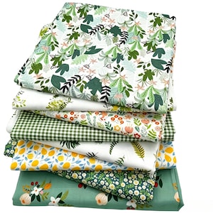Op de afbeelding: Een stapel van zeven gevouwen stoffen met diverse patronen, waaronder groen-witte botanische prints, een groen-wit gingham ruitpatroon, gele citroenmotieven en een saliegroene achtergrond met bloemillustraties in wit en perzik.