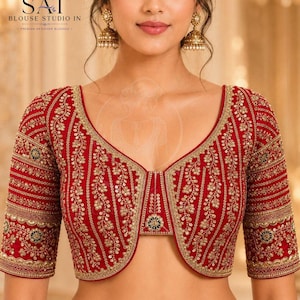 Puede incluir: Una blusa de color rojo intenso con intrincados bordados dorados, lentejuelas y abalorios. La prenda presenta un escote en V, mangas hasta el codo y un panel frontal estructurado con un motivo circular central y patrones florales verticales.