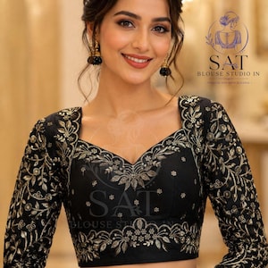 May include: A black blouse featuring long sleeves with intricate gold floral embroidery. The garment has a sweetheart neckline and a cropped hemline. The text SAT BLOUSE STUDIO IN is visible in the upper right corner of the image.