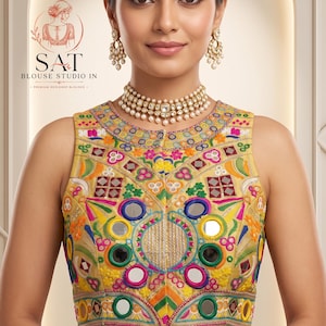 May include: A sleeveless gold-toned blouse featuring intricate multi-coloured embroidery, circular mirror embellishments, and a row of white shell-like beads along the hem. The garment includes a round neckline and a front closure with visible text.