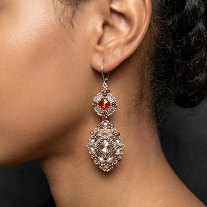 May include: A dangling earring featuring a small square red crystal top section and a larger diamond-shaped bottom section. Both parts are intricately beaded with metallic silver, bronze, and clear crystals, suspended from a silver-toned metal hook.