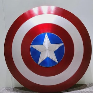 May include: A circular shield featuring a concentric design with a metallic red outer ring, a silver middle ring, and a central blue circle containing a large, five-pointed silver star. The surface has a smooth, reflective finish throughout.