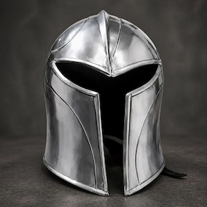 Pode incluir: Um capacete de metal prateado polido com uma cúpula lisa e arredondada, uma crista central e uma ampla abertura de viseira horizontal que se curva para baixo até uma fenda vertical na frente, criando uma peça de proteção brilhante e elegante.