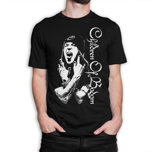 Op de afbeelding: Een zwart t-shirt met korte mouwen en een witte grafische print van een persoon met een muts, open mond en opgeheven handen. De tekst Children Of Bodom is verticaal in een gestileerd wit lettertype aan de rechterkant gedrukt.