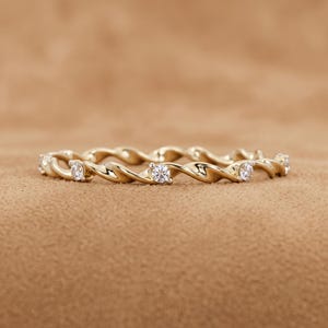 Peut inclure: Une bague en or avec un design de bande torsadée semblable à une corde. La bande est agrémentée de plusieurs petites pierres rondes, claires et facettées, serties à intervalles réguliers le long de la structure métallique, créant un aspect texturé.
