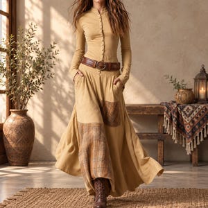 May include: A long-sleeved tan dress featuring a button-down bodice, a brown leather belt with a circular buckle, and a full-length skirt with integrated plaid fabric panels on the front. The garment is paired with brown lace-up boots.