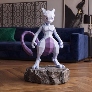 May include: A low-poly geometric figurine of the character Mewtwo, featuring a light lavender and purple color scheme. The figure stands in a bipedal pose with a long tail, positioned on a textured, gray, rock-like base with sharp, angular facets.