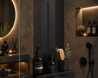 Op de afbeelding: Een matzwart douche-rekje voor over een glazen wand, voorzien van een verticale beugel, een platte opbergplank met geïntegreerde sleuven voor scheermesjes en een haak voor accessoires. Het rekje bevat twee donkere flessen en een beker met borstel.