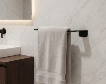 Op de afbeelding: Een matzwarte metalen handdoekhouder gemonteerd op een witte marmeren muur, met daaraan een gevouwen lichtbeige katoenen handdoek. De handdoekhouder heeft een rechthoekige muurplaat en een horizontale stang voor functionele badkamerinrichting.