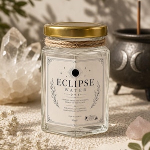 May include: A hexagonal glass jar with a gold lid and twine wrap, featuring a label that reads ECLIPSE WATER, CHARGED UNDER THE POWERFUL ENERGY OF THE ECLIPSE, FOR RITUALS, CLEANSING, MANIFESTING, INTENTION, 100% NATURAL, and 50ml.