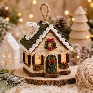 Può includere: Un ornamento a forma di casa realizzato all'uncinetto con facciata color crema, tetto verde scuro con bordo bianco, porta verde scuro con ghirlanda e fiocco rosso, e persiane marroni. La casa include un camino e un occhiello per appenderla.