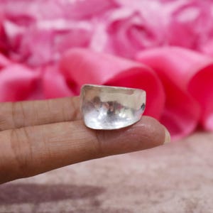 May include: A wide, polished silver ring with a smooth, slightly curved surface. The band features a reflective, metallic finish that catches the light, showcasing a simple, unadorned design with a broad, rounded front profile and a solid construction.
