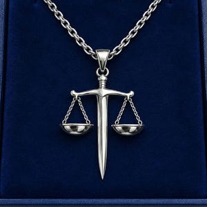 May include: A silver-toned metal pendant necklace featuring a central sword design integrated with a pair of balanced scales. The pendant hangs from a matching silver-toned link chain, showcasing a polished, reflective finish on the metal surface.