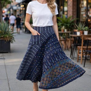 Puede incluir: Una camiseta blanca de manga corta combinada con una falda midi de talle alto. La falda presenta una base azul oscuro con una mezcla de rayas verticales blancas en la cintura y el bolsillo, y un complejo patrón geométrico en azul, verde y oro.