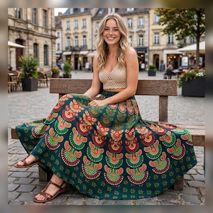 May include: A beige crochet crop top with a V-neckline and a long, flowing dark green skirt featuring a repeating fan-shaped pattern in shades of orange, yellow, and green. The skirt has a wide, pleated hem and is paired with brown sandals.