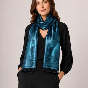 May include: A rectangular scarf in a deep teal color featuring a repeating pattern of elephants and intricate floral motifs. The scarf has a smooth, satin-like finish and is finished with short black fringe along the bottom edges.