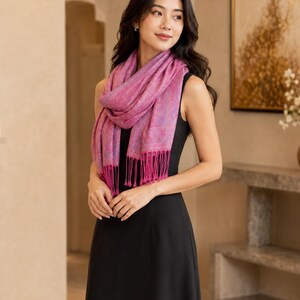 May include: A vibrant magenta pashmina scarf featuring an intricate, subtle tonal paisley pattern and delicate fringe detailing at the ends. The scarf is draped loosely around the neck, showcasing its soft texture and rich, deep pink color palette.