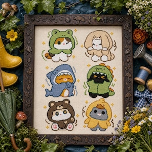 May include: A framed cross-stitch embroidery on light beige fabric featuring six cartoon animals wearing costumes: a frog, a rabbit, a shark, a dinosaur, a bear, and a duck. The dark wooden frame is decorated with small carved umbrellas and leaves.