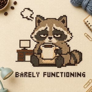 May include: A cross-stitch pattern on cream fabric featuring a tired raccoon sitting at a desk with a computer, holding a coffee mug. Above the raccoon is a thought bubble, and below is the text BARELY FUNCTIONING in dark brown block letters.
