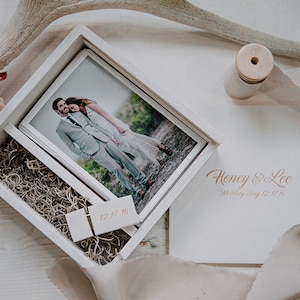 May include: A white wooden box with a photo of a couple, surrounded by decorative elements. The box contains photos and decorative filler. The text "Honey & Lee Wedding Day 12.17.16" is visible on the envelope.