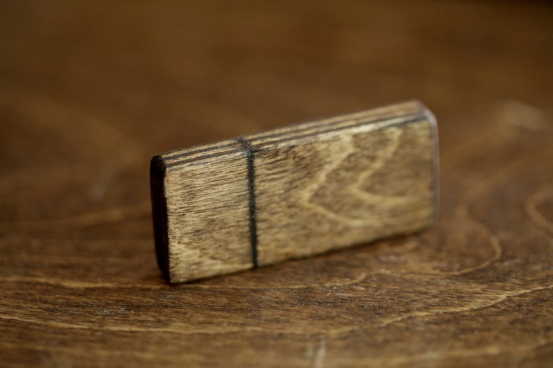 Puede incluir: Una peque&ntilde;a caja rectangular de madera con una mancha marr&oacute;n oscura. La caja tiene un patr&oacute;n de veta de madera natural y una fina l&iacute;nea negra que recorre el centro.
