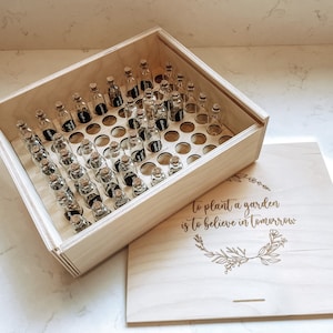 May include: A wooden box with a lid, filled with small glass bottles. The lid has an engraved quote: "To plant a garden is to believe in tomorrow."