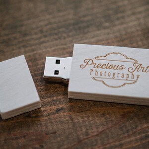 Puede incluir: Unidad USB de madera blanca con un logotipo grabado en oro que dice "Precious Art Photography".