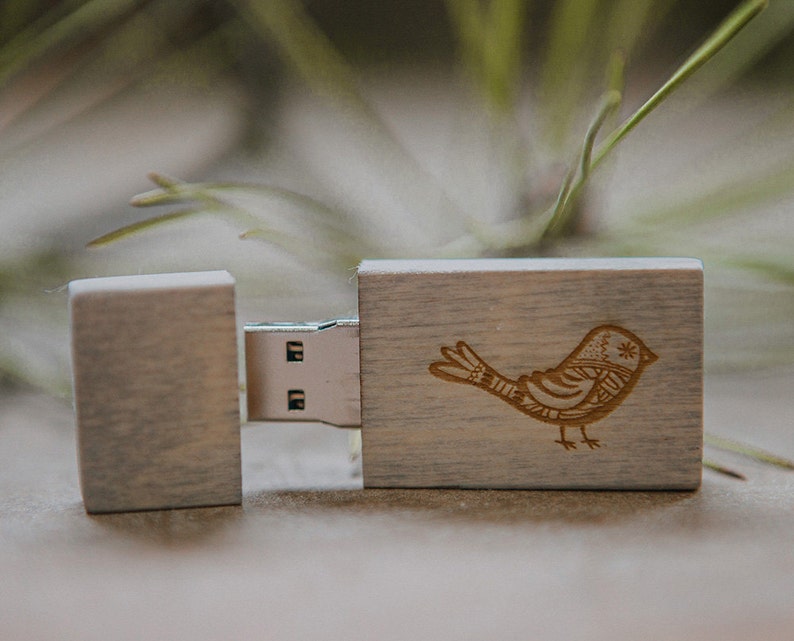 Puede incluir: Una memoria USB de madera con un dise&ntilde;o de p&aacute;jaro grabado en la parte delantera. La memoria est&aacute; cerrada y el puerto USB es visible.
