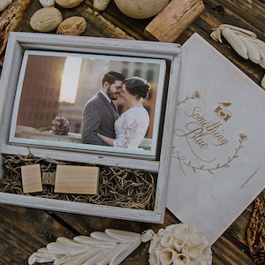 May include: A wooden box with a framed photograph of a couple, a wooden USB drive, and a matching card with the text "Something Blue." The box is filled with dried grass and sits on a wooden surface.