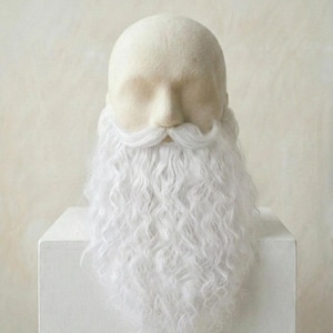 Peut inclure: Une tête de mannequin en feutre blanc dotée d'une longue barbe blanche bouclée et d'une moustache assortie. Les traits du visage sont lisses et sans détails, avec les longs poils blancs texturés descendant du menton et de la lèvre supérieure.