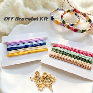 May include: A DIY Bracelet Kit featuring two white cardboard spools wrapped with multi-colored embroidery thread, two finished woven bracelets with small gold beads, and a small pile of loose gold-toned seed beads on a white surface.