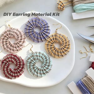 May include: A DIY Earring Material Kit featuring five circular earrings with spiral patterns in pink, purple, yellow, red, and light blue, each with gold-toned hooks. The kit includes spools of colored thread and additional metal earring hooks.