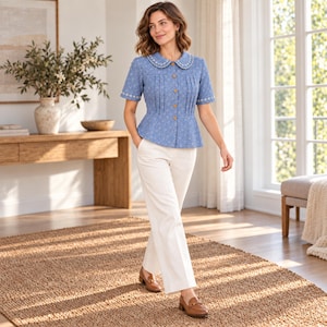 Könnte beinhalten: Eine blaue kurzärmelige Bluse mit kleinem Blumenmuster, rundem Kragen mit weißer Bogenstickerei, vertikalen Falten auf der Vorderseite und braunen Knöpfen. Die Bluse wird mit einer weißen Hose und braunen Leder-Loafern kombiniert.