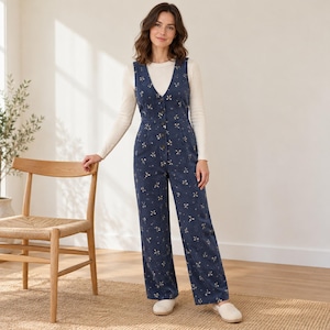 Könnte beinhalten: Ein ärmelloser Jumpsuit in Marineblau mit weißem Blumenmuster, V-Ausschnitt und Knopfleiste vorne, getragen über einem cremefarbenen Langarmshirt mit hellen Schlupfschuhen.