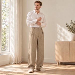 Könnte beinhalten: Ein langärmeliges weißes Hemd mit Kragen und Manschetten, kombiniert mit einer hoch taillierten, weit geschnittenen Hose in hellem Beige mit dezentem vertikalem Nadelstreifenmuster, Knopfverschluss vorne und Bundfalten.