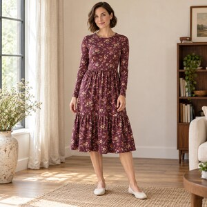 Könnte beinhalten: Ein langärmeliges Midikleid in tiefem Burgunderrot mit einem sich wiederholenden Blumenmuster in Creme-, Rosa- und gedeckten Grüntönen. Das Kleid hat einen Rundhalsausschnitt, ein figurbetontes Oberteil und einen gestuften Rock, der unter die Knie reicht.