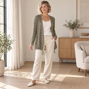 Puede incluir: Un cárdigan de manga larga en color verde oliva con un estampado floral blanco, que presenta un dobladillo con cordón. El cárdigan se lleva sobre una camiseta de tirantes blanca lisa y se combina con pantalones rectos beige claro y zapatos sin cordones.