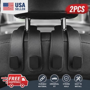May include: Two black leather-textured car headrest hooks designed to hang over the metal posts of a vehicle seat. Each strap features a matte black hook at the bottom. The text 2PCS is visible in the upper right corner of the image.
