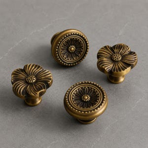 May include: Four antique brass cabinet knobs. Two knobs feature a circular design with a central daisy-like pattern and a beaded border. The other two knobs are shaped like five-petaled flowers with a textured center and defined petal grooves.