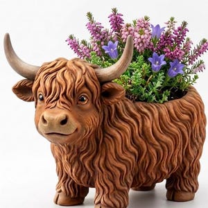 May include: A brown highland cow-shaped planter featuring a textured, shaggy coat and curved horns. The planter is filled with a vibrant arrangement of purple heather flowers and small blue bell-shaped blossoms, creating a decorative display.