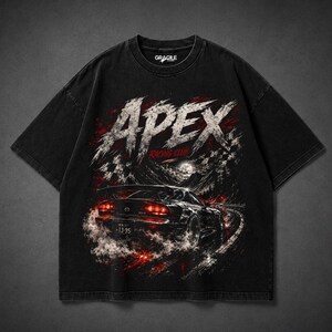May include: A black short-sleeve t-shirt featuring a graphic print of a sports car on a winding road at night. The text APEX RACING CLUB is printed in large, distressed white letters above the car. The design includes red accents and smoke.