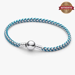 May include: A bracelet featuring a woven design of bright blue cord intertwined with polished silver-toned metal links. The piece includes a smooth, spherical silver-toned clasp mechanism at the center, creating a continuous circular shape.