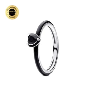 May include: A ring featuring a smooth black band with a polished silver interior and a single black heart-shaped stone set in a silver prong setting. The design is sleek and minimalist, showcasing a contrast between the dark exterior and metallic inner.