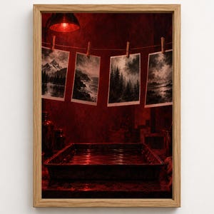 May include: A framed wall art print depicting a darkroom scene bathed in red light. Four black and white landscape photographs hang from a string with wooden clothespins above a rectangular developing tray filled with liquid, all set in a wooden frame.