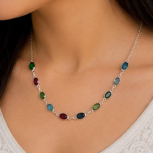 Peut inclure: Un collier en chaîne argentée orné d'une série de petites pierres précieuses ovales de différentes couleurs, notamment rouge, bleu et vert. Les pierres sont serties individuellement le long de la fine chaîne métallique, créant un motif espacé.