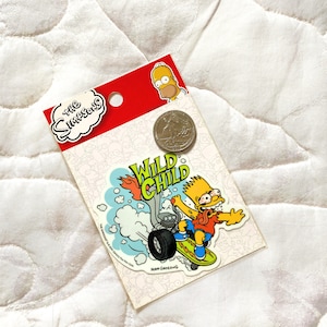 May include: A yellow sticker featuring Bart Simpson riding a motorcycle with the words "Wild Child" in a yellow and green font. The sticker is on a white background with a red border and a small image of Bart Simpson in the top right corner.