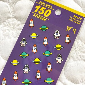 Op de afbeelding: Een vel met 150 stickers met een ruimtethema met raketten, astronauten en planeten op een paarse achtergrond. De tekst "CHOA CHOA 150 STICKER" staat bovenaan het vel. De tekst "SPACE korean mart mini sticker" staat rechtsboven op het vel.