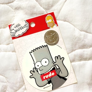 May include: A white sticker with a black and white cartoon image of Bart Simpson from The Simpsons. Bart is wearing a black shirt with the word "rude" in red letters across the front. The sticker is on a white background with a small image of Homer Simpson in the top right corner.