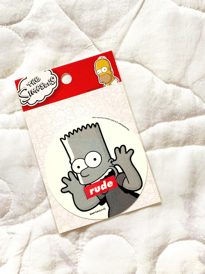 May include: A white sticker with a black and white image of Bart Simpson from The Simpsons cartoon. Bart is wearing a black shirt with the word "rude" printed in red on it. He is making a rude gesture with his hands. The sticker is on a white background.