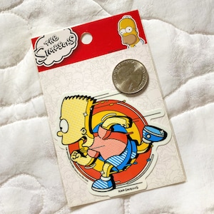 May include: A yellow and blue sticker featuring a cartoon character running in a circle. The character is wearing a red and blue shirt and blue pants. The sticker is labeled "The Simpsons" and "Matt Groening".